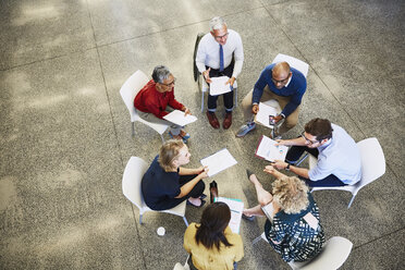 Business people discussing paperwork in meeting circle - HOXF03063