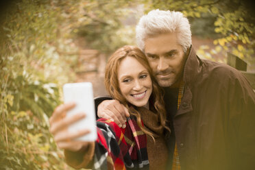 Paar, das sich umarmt und ein Selfie mit einem Fotohandy im Garten macht - HOXF03098