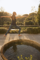 Frau übt Yoga-Krieger 2-Pose auf Herbst-Terrasse mit Whirlpool - HOXF03103