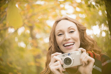 Portrait enthusiastic woman with digital camera under autumn trees - HOXF03106