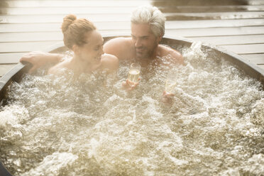 Lächelndes Paar trinkt Champagner im Whirlpool auf der Terrasse - HOXF03112