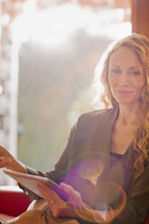 Portrait smiling woman using digital tablet in sunny window - HOXF03119