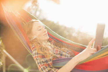 Frau entspannt sich in sonniger Hängematte mit digitalem Tablet - HOXF03122