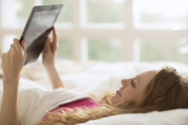 Frau liegt im Bett und benutzt ein digitales Tablet - HOXF03125