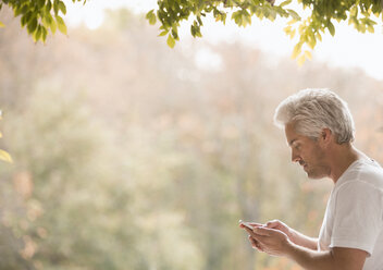 Mann schreibt SMS mit Handy auf Terrasse - HOXF03136