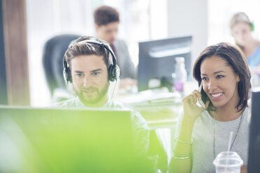 Kreative Geschäftsleute mit Kopfhörern, die mit dem Handy telefonieren und einen Computer im Büro benutzen - HOXF03182