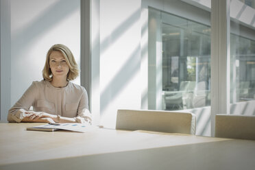 Portrait confident businesswoman sitting at sunny conference table - HOXF03205