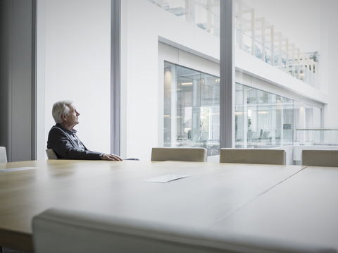Nachdenklicher älterer Geschäftsmann schaut aus dem Fenster des Konferenzraums, lizenzfreies Stockfoto
