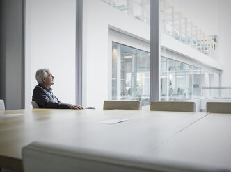 Pensive senior businessman looking out conference room window - HOXF03209