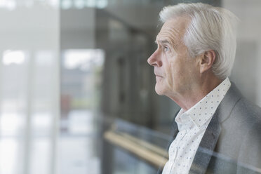 Pensive businessman looking out office window - HOXF03227