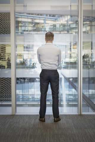 Geschäftsmann steht am Bürofenster mit Blick auf das Atrium, lizenzfreies Stockfoto