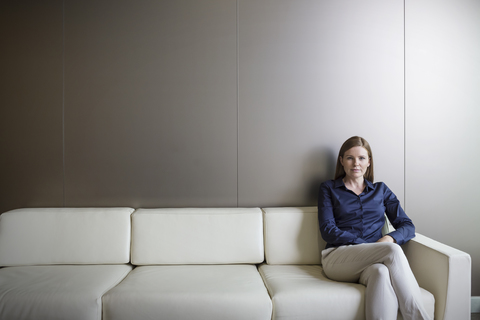 Porträt einer selbstbewussten Geschäftsfrau mit gekreuzten Beinen auf dem Sofa, lizenzfreies Stockfoto