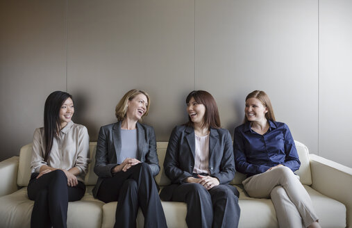 Lächelnde Geschäftsfrauen, die sich in einer Reihe auf dem Sofa unterhalten - HOXF03256