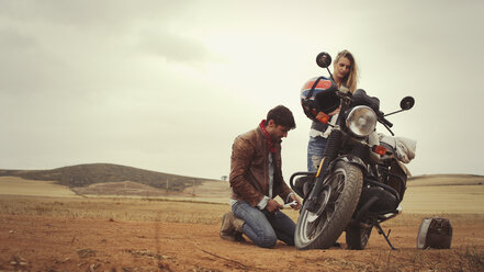 Junges Paar repariert Motorrad in einem abgelegenen Feld auf dem Land - HOXF03321