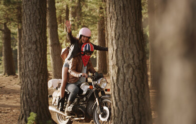 Exuberant young woman riding motorcycle in woods - HOXF03323