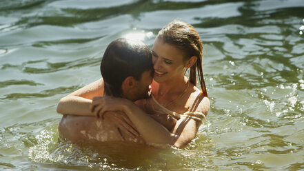 Affectionate couple hugging and swimming in sunny lake - HOXF03327