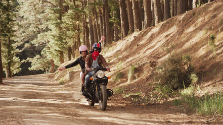 Übermütige junge Frau fährt Motorrad auf unbefestigtem Weg im Wald - HOXF03334