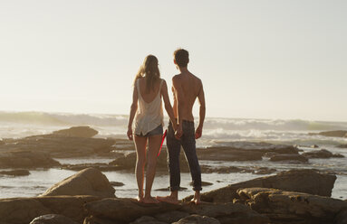 Junges Paar, das sich an den Händen hält und auf das Meer blickt - HOXF03337