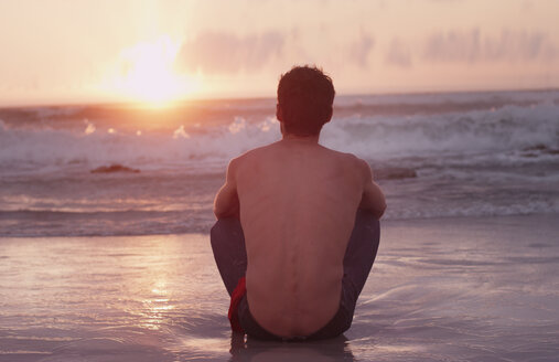 Nachdenklicher junger Mann am Strand bei Sonnenuntergang über dem Meer - HOXF03344