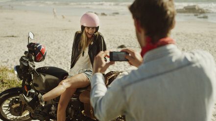 Junger Mann fotografiert Frau auf Motorrad am Strand - HOXF03345