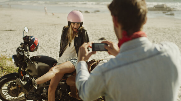 Junger Mann fotografiert Frau auf Motorrad am Strand - HOXF03345