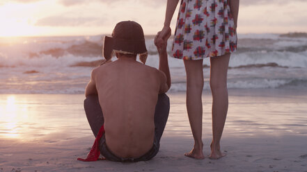 Young couple holding hands on beach at sunset - HOXF03348