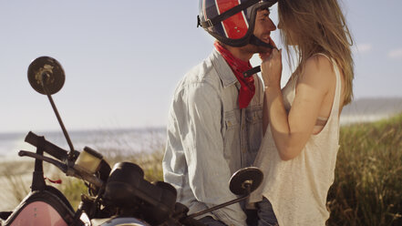 Verliebtes junges Paar auf einem Motorrad mit Strand im Hintergrund - HOXF03349