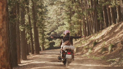 Übermütige junge Frau fährt Motorrad auf unbefestigtem Weg im Wald, lizenzfreies Stockfoto