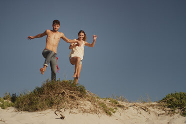 Verspieltes junges Paar springt am Sandstrand - HOXF03354