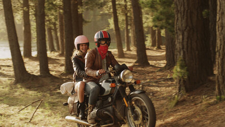 Young couple riding motorcycle in woods - HOXF03356