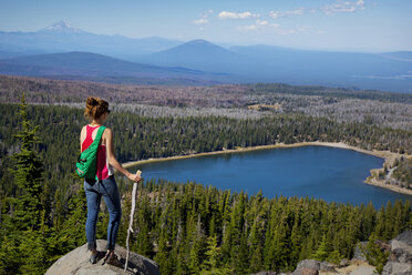 Female hiker looking at lake and trees while standing on top of cliff - CAVF00016