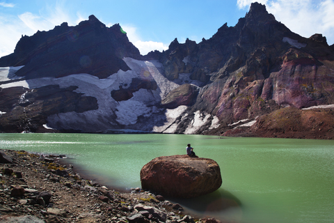 Fernansicht eines Wanderers auf einem Felsen am Seeufer vor den Bergen, lizenzfreies Stockfoto