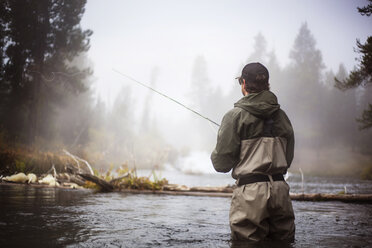 Rear view of hiker fishing in lake during foggy weather - CAVF00036