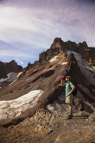 Wanderer trinkt, während er auf einem Berg gegen den Himmel steht, lizenzfreies Stockfoto