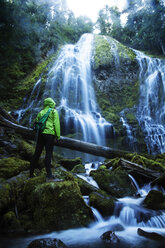 Rückansicht einer Wanderin, die einen Wasserfall betrachtet, während sie auf einem Felsen im Wald steht - CAVF00053