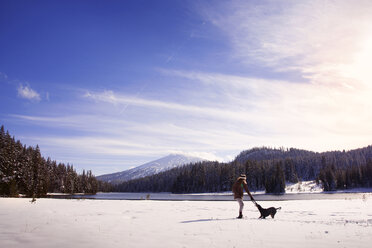 Woman playing with dog on snow covered field against sky - CAVF00068