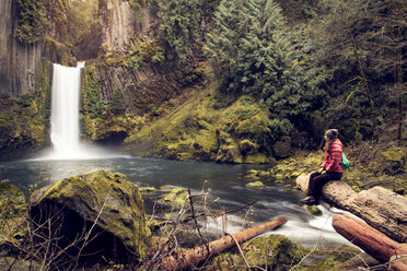 Wanderer betrachtet einen Wasserfall, während er auf einem Felsen im Wald sitzt - CAVF00089