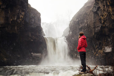 Wanderin betrachtet einen Wasserfall, während sie auf einem Felsen im Wald steht - CAVF00114