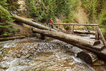 Frau steht auf einer Brücke über einen Fluss im Wald - CAVF00131