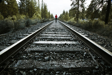 Rückansicht einer Frau, die auf einem Bahngleis im Wald läuft - CAVF00137