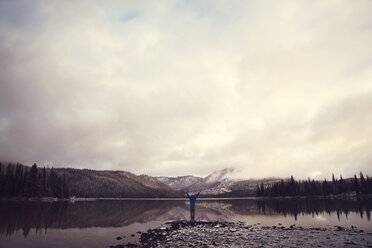 Man standing with arms outstretched at Sparks Lake against cloudy sky - CAVF00149