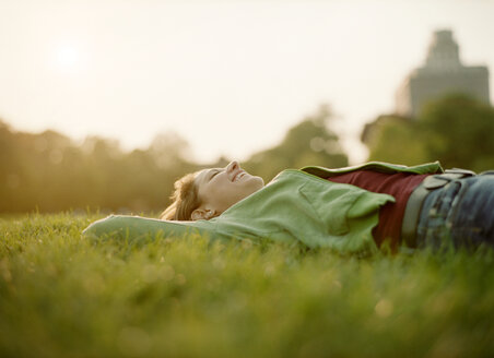 Fröhliche Frau auf einer Wiese liegend gegen den Himmel an einem sonnigen Tag - CAVF00156