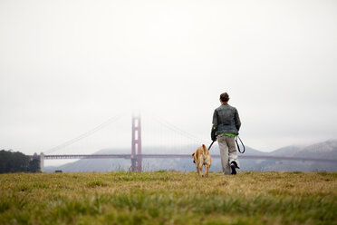 Rear view of woman and dog walking on grassy field at Golden Gate Park - CAVF00169