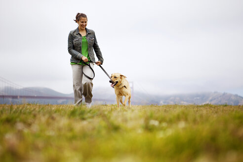 Glückliche Frau mit Hund auf einer Wiese vor bewölktem Himmel - CAVF00171