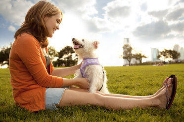 Seitenansicht einer Frau, die mit einem Hund auf einer Wiese vor dem Himmel spielt - CAVF00181