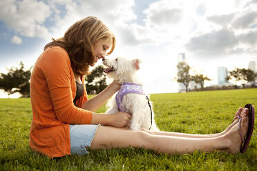 Glückliche Frau spielt mit Hund auf einer Wiese an einem sonnigen Tag - CAVF00182