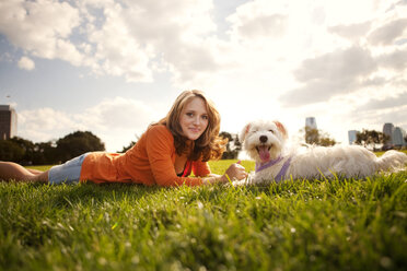 Portrait of young woman lying with dog on grassy field against sky - CAVF00183