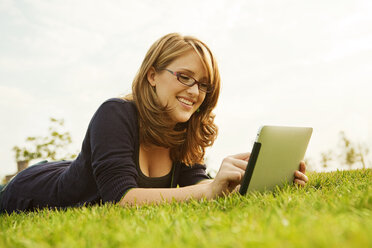 Smiling woman using digital tablet while lying on grassy field - CAVF00195