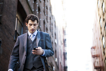 Low angle view of businessman using smart phone against buildings - CAVF00202