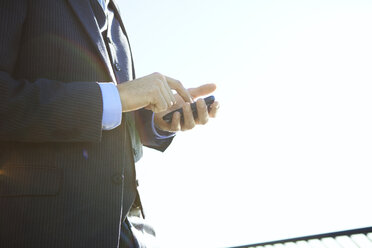 Side view of businessman using smart phone against clear sky - CAVF00203